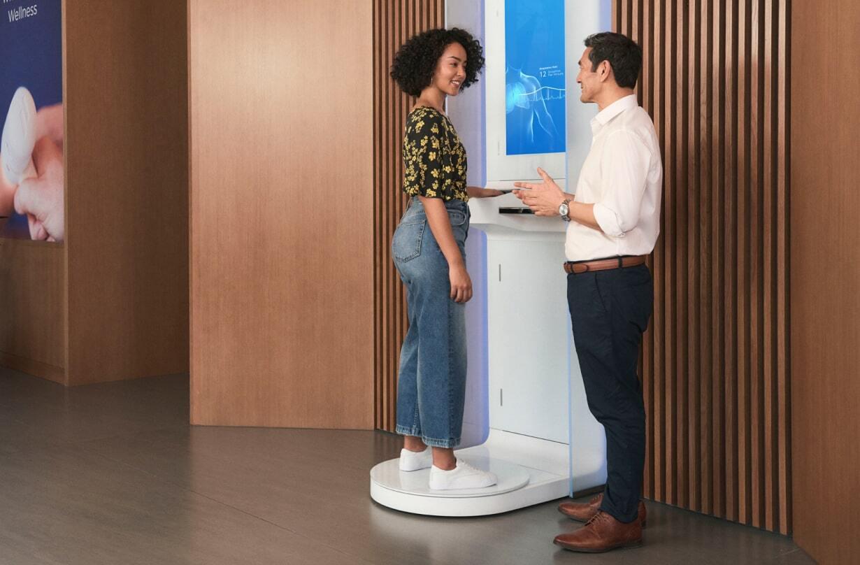 Woman stands on Forward's body scanner while talking with a doctor.