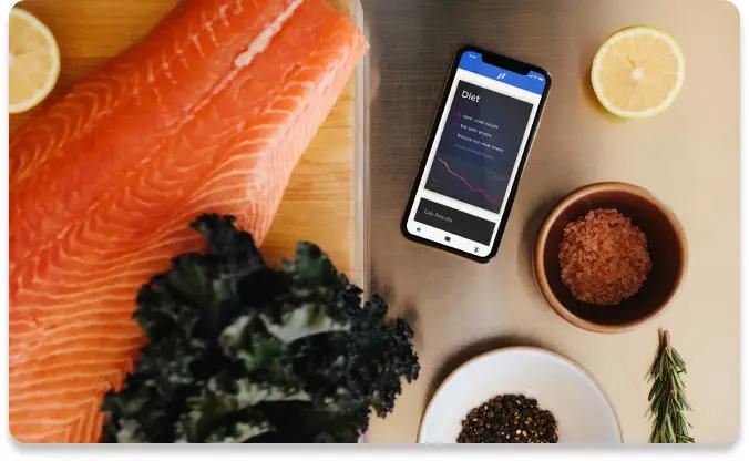 Image showing healthy food options like salmon and kale with a phone showing Diet metrics.
