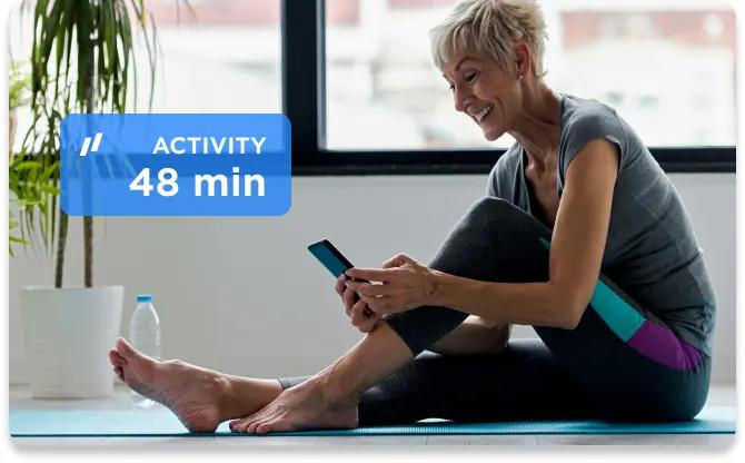 Older woman on a mat in athletic clothing looking at her phone after exercising.