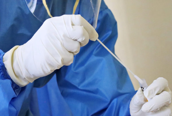 doctor puts cotton swab in vial while wearing gloves