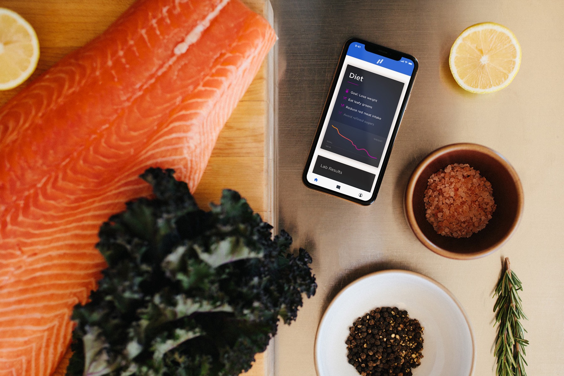 raw salmon and leafy green sit on table next to a phone with diet on screen