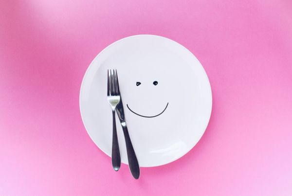 knife and fork sit on white plate with a smiley face on a pink background