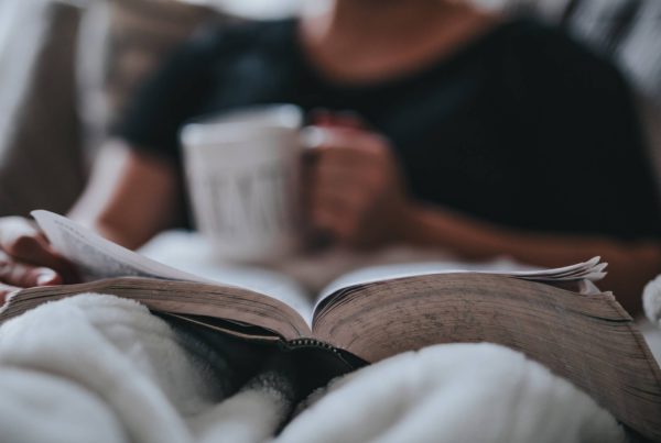 person sits with a mug and a book in their lap