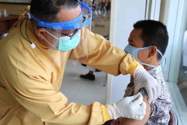 medical professional with a face guard gives man with a cloth mask a vaccine