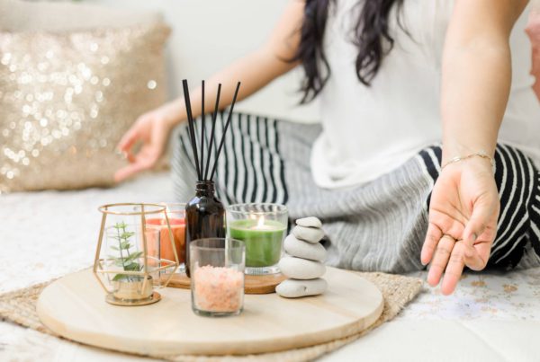 woman meditates with her legs crossed and palms up. tray of incense, salts, and candles are in front of her