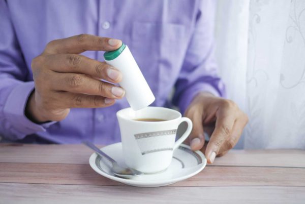 person in a purple shirt holds a device for diabetes over a cup of tea