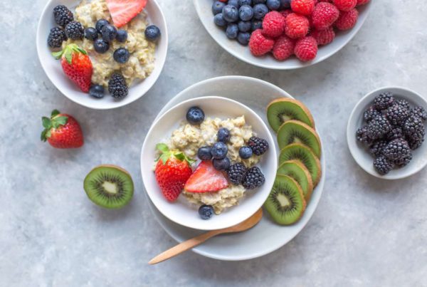 4 white bowls full of berries, kiwi, and oatmeal