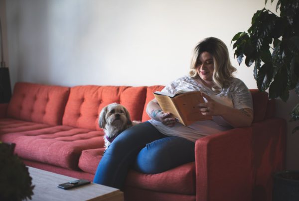 woman reads book on a read couch with a dog sitting next to her