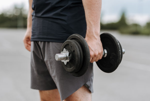 man in a black shirt and gray shorts holding dumbbell in one hand