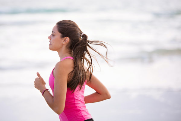 young woman with a ponytail and in a hot pink exercise tank top running on the beach
