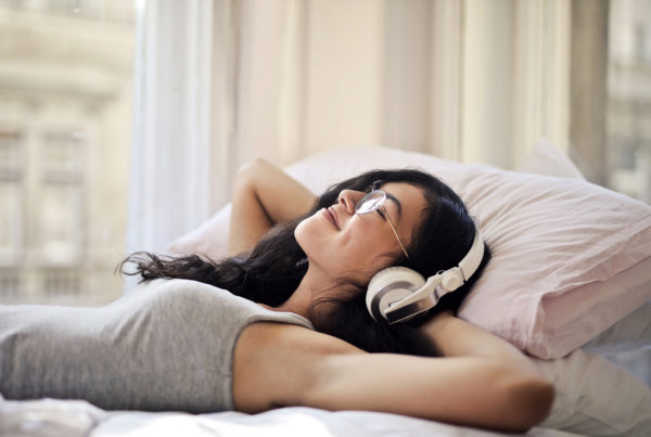 woman laying on bed with hands behind her head listening to music with headphones