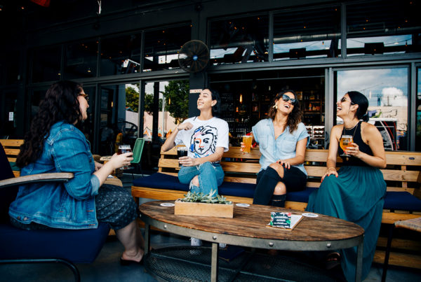 group of four women sitting outside drinking beer and talking
