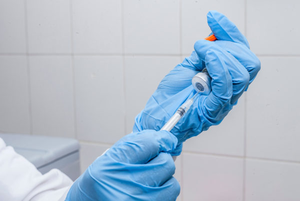 medical professional in blue gloves fills needle with vaccine from vial