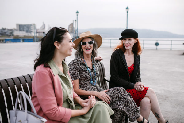 three middle aged women sitting on a bench smiling at each other