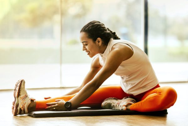 woman in white tank top and orange leggings stretching on a mat on the floor