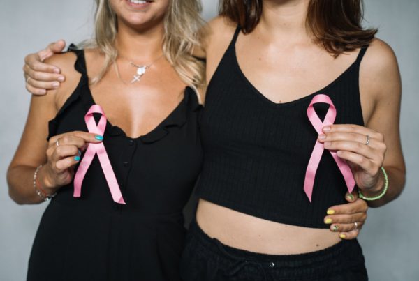 two women in black clothes with their arms around each other holding pink breast cancer ribbons